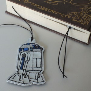 May include: A white and blue embroidered R2-D2 bookmark with a black string.