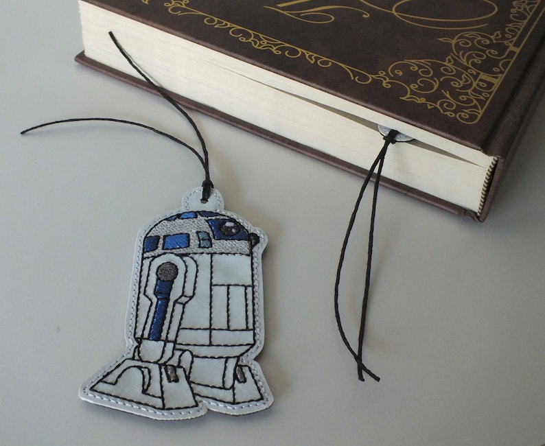 May include: A white and blue embroidered R2-D2 bookmark with a black string.