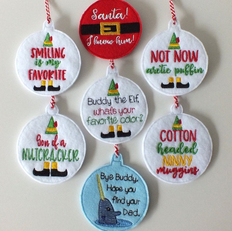 May include: Set of 7 felt Christmas ornaments with elf and holiday-themed designs. The ornaments feature phrases like "Smiling is my favorite", "Son of a Nutcracker", "Santa! I know him!" and "Bye Buddy. Hope you find your Dad."