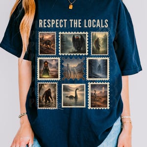 Puede incluir: Camiseta azul marino con el texto "RESPECT THE LOCALS" sobre una cuadrícula de sellos postales de estilo vintage. Cada sello presenta una criatura críptica diferente, como Bigfoot y el monstruo del lago Ness.