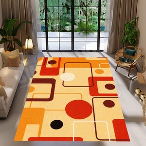 May include: A rectangular rug with a geometric pattern in orange, red, brown, and cream. The design features squares, circles, and lines. The rug is placed on a light-coloured floor in a well-lit room.