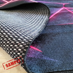 Puede incluir: Primer plano de una alfombra con un dise&ntilde;o geom&eacute;trico en tonos azules, morados y rosas. Se ve la parte inferior de la alfombra, mostrando un patr&oacute;n de cuadros blancos y negros. La palabra "SAMPLE" est&aacute; estampada en la alfombra.