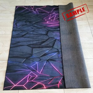Puede incluir: Una alfombra rectangular con un dise&ntilde;o geom&eacute;trico en tonos grises, azules y morados. El patr&oacute;n presenta formas angulares con l&iacute;neas rosas y moradas de estilo ne&oacute;n. La alfombra est&aacute; parcialmente enrollada, revelando un respaldo gris texturizado. La palabra "SAMPLE" est&aacute; estampada en la alfombra.