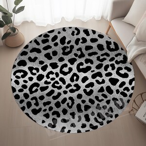 Könnte beinhalten: Ein runder Teppich mit Leopardenmuster. Der Teppich hat einen grauen Hintergrund mit schwarzen Flecken, wodurch ein auffälliges Muster entsteht. Er liegt auf einem hellen Holzboden.