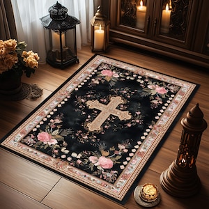 May include: A rectangular black rug with a floral and cross design. The rug features a large, ornate cross in the center, surrounded by pink roses and other flowers. The border is a mix of cream, pink, and brown. The rug is placed on a wooden floor.