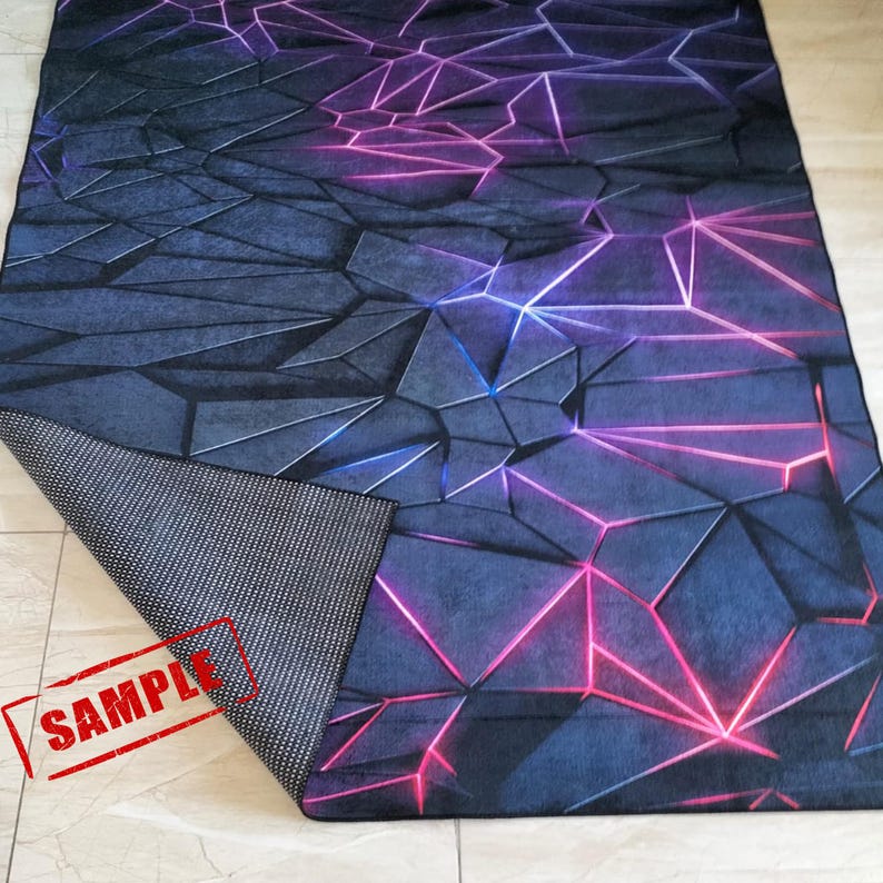 Puede incluir: Una alfombra rectangular con un dise&ntilde;o geom&eacute;trico. La alfombra presenta un fondo azul oscuro y gris con un patr&oacute;n de formas interconectadas resaltadas por l&iacute;neas rosas y azules. Se ve la parte inferior de la alfombra, que muestra un material gris oscuro texturizado.