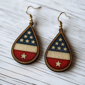 Op de afbeelding: Een paar traanvormige houten oorbellen met een rood, wit en blauw Amerikaans vlagontwerp. De oorbellen hebben gouden haken.