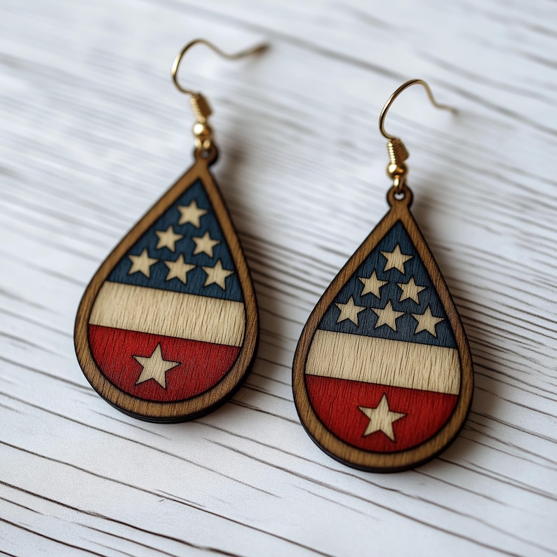 Op de afbeelding: Een paar traanvormige houten oorbellen met een rood, wit en blauw Amerikaans vlagontwerp. De oorbellen hebben gouden haken.