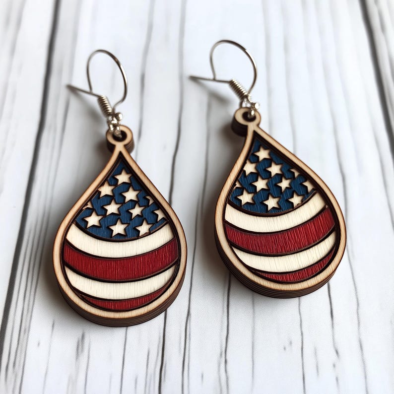 Op de afbeelding: Een paar houten, traanvormige oorbellen met een Amerikaans vlagontwerp. De oorbellen zijn rood, wit en blauw geverfd.