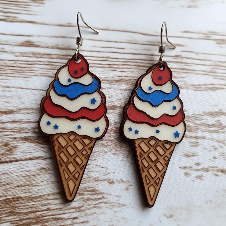 Op de afbeelding: Een paar houten ijshoorntjes oorbellen met rood, wit en blauw ijs en een kers op de top. De oorbellen zijn versierd met blauwe sterren.