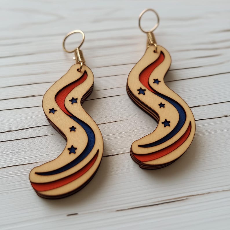 Op de afbeelding: Een paar houten oorbellen met een rood, wit en blauw ontwerp. De oorbellen zijn gevormd als een golvende lijn met uitgesneden sterren. De oorbellen zijn bevestigd aan gouden haken.