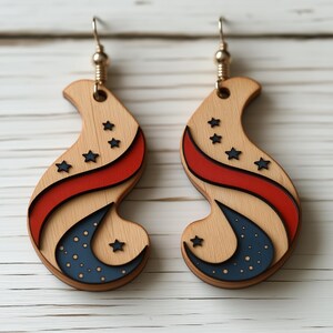 Op de afbeelding: Een paar houten oorbellen met een rood, wit en blauw ontwerp. De oorbellen zijn gevormd als een halve maan met sterren en een rode streep.