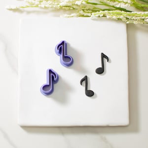May include: A white surface with three purple and two black music note cookie cutters. The cookie cutters are arranged in a random pattern.