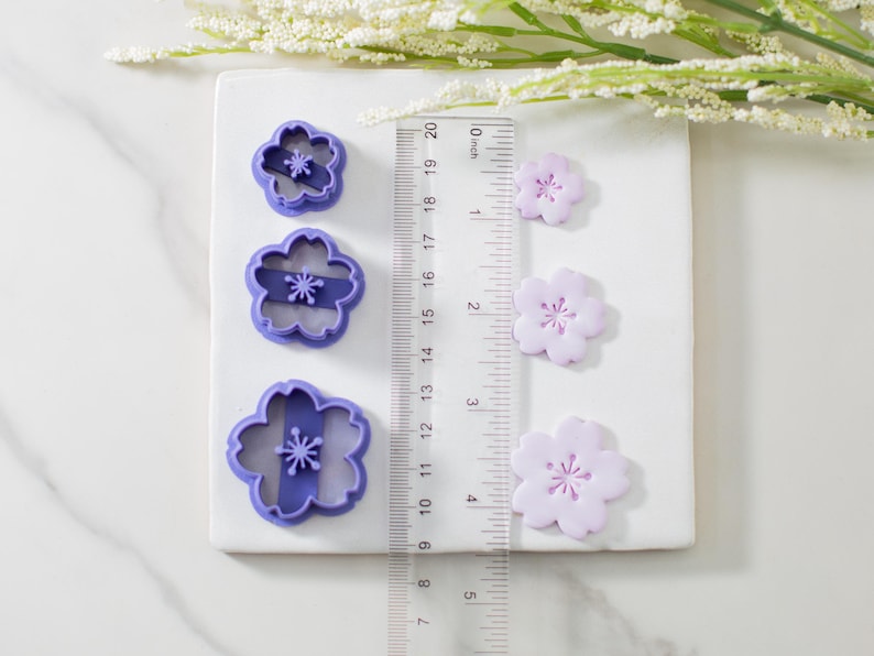 May include: Set of three purple plastic flower cookie cutters with three matching purple fondant flowers of different sizes. The cutters are 1.5 inches, 2 inches, and 2.5 inches in diameter.