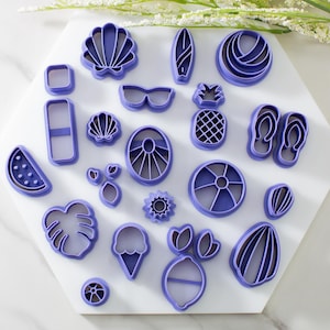 May include: A set of 18 purple plastic cookie cutters shaped like various summer-themed objects, including a pineapple, watermelon, sunglasses, flip flops, and a beach ball.