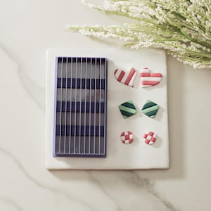 May include: A white ceramic tile with a purple plastic grid and five polymer clay shapes: two red and white striped hearts, two green and white striped diamonds, and two red and white checkered circles.