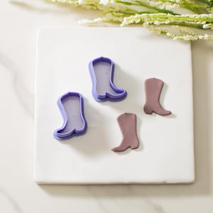 May include: Three purple plastic cookie cutters shaped like cowboy boots, and two brown fondant cowboy boots.