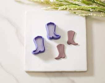 Può includere: Tre tagliapasta di plastica viola a forma di stivali da cowboy e due stivali da cowboy di pasta di zucchero marroni.