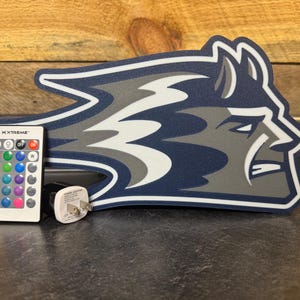 May include: A blue and gray mascot head shaped light with a remote control and power adapter. The remote control has a button labeled "XTREME" and has multiple colored buttons.