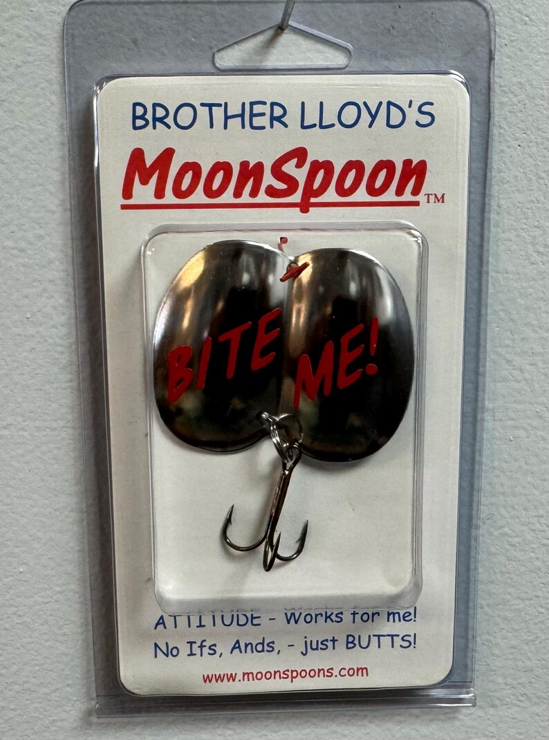Puede incluir: Un se&ntilde;uelo de pesca plateado con las palabras "Bite Me!" en letras rojas. El se&ntilde;uelo est&aacute; empaquetado en una bl&iacute;ster de pl&aacute;stico transparente con una tarjeta blanca que dice "Brother Lloyd's MoonSpoon.  ATTITUDE - Works for me! No Ifs, Ands, - just BUTTS! www.moonspoons.com"