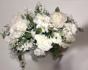 May include: A white floral arrangement with a variety of white flowers, including roses, hydrangeas, and peonies. The arrangement is accented with greenery and a string of pearls.