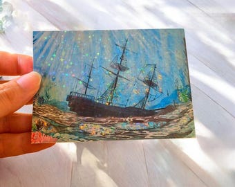Könnte beinhalten: Ein rechteckiger Aufkleber mit einem dunkelbraunen Segelschiff, das auf dem Meeresboden liegt. Die Szene zeigt blaues Wasser, Korallen und eine holografische Oberfläche, die einen schimmernden Effekt kleiner Sterne erzeugt.