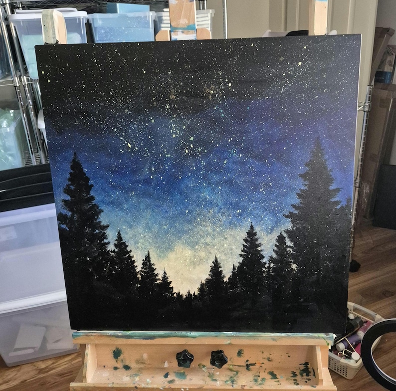 May include: A square canvas painting depicting a night sky filled with white and yellow star-like speckles above a dark silhouette of a dense pine forest. The sky transitions from a deep black at the top to a lighter blue and white near the horizon.