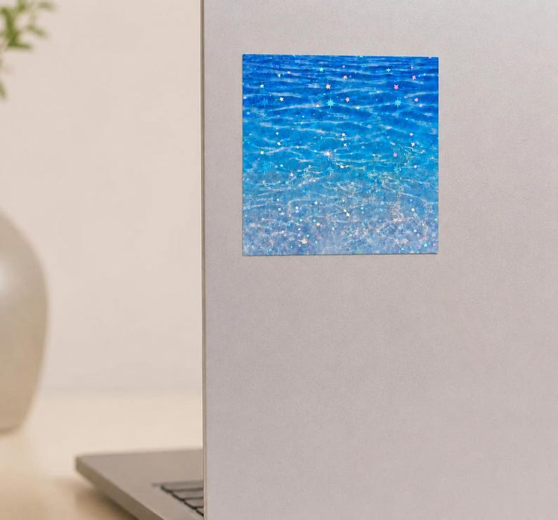 K&ouml;nnte beinhalten: Ein quadratischer Aufkleber mit einer leuchtend blauen Wasseroberfl&auml;che, die einen Farbverlauf von tiefem Marineblau bis zu hellem Cyan aufweist. Das Design ist mit holografischen Sternen &uuml;berlagert, die schimmernde Lichtreflexe erzeugen.