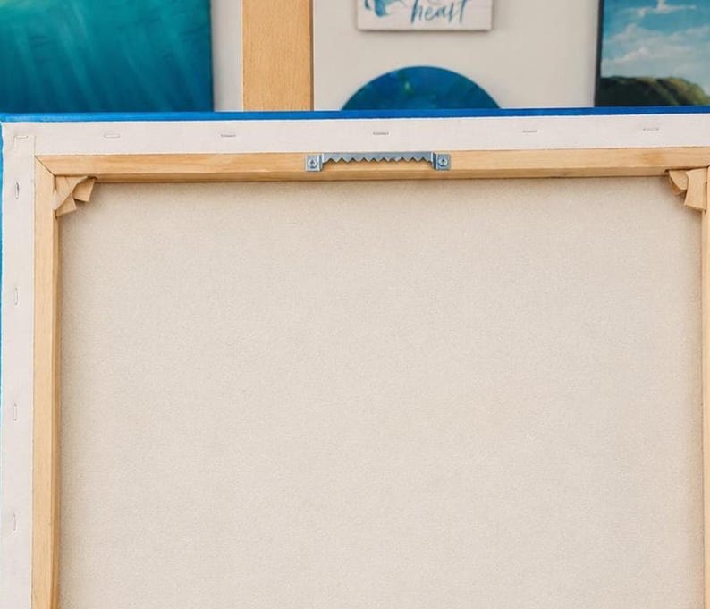 May include: The back of a rectangular canvas stretched over a light-colored wooden frame. The canvas is secured with staples along the edges and features a silver-toned metal sawtooth hanger centered on the top wooden bar for wall mounting.