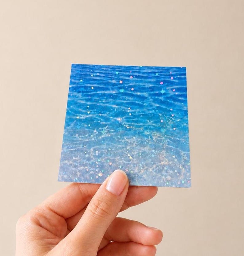 K&ouml;nnte beinhalten: Ein quadratischer Aufkleber mit einem leuchtend blauen Wasseroberfl&auml;chenmuster und holografischem Finish. Das Design zeigt kr&auml;uselnde Wellen in Azur- und Cyan-T&ouml;nen, die mit einer Streuung kleiner, schimmernder sternf&ouml;rmiger Symbole &uuml;berlagert sind.