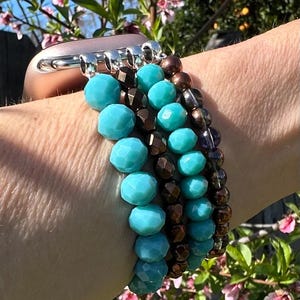 May include: A turquoise and brown beaded bracelet with a silver clasp. The bracelet is worn on a person's wrist.