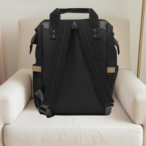 Pu&ograve; includere: Zaino nero per pannolini con spalline regolabili e dettagli beige. Lo zaino ha una chiusura con cerniera e diverse tasche.