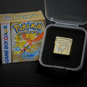 May include: A gold-coloured Game Boy Color cartridge featuring a picture of the Pokémon character, Articuno, on the front. The cartridge is in a clear plastic case with a black foam interior. The text on the cartridge reads "GAME BOY COLOR" and "POKÉMON GOLD VERSION".