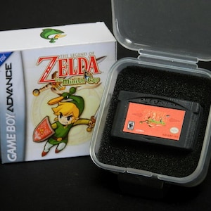 May include: A black Game Boy Advance game cartridge case with a clear plastic lid. The case contains a Game Boy Advance game cartridge for The Legend of Zelda: The Minish Cap. The cartridge is black with a red label featuring the game's title and logo.