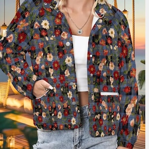 Puede incluir: Chaqueta a cuadros azul con un estampado floral de flores rojas, blancas y melocotón. La chaqueta tiene cuello blanco, ribete de bolsillo blanco y botones plateados. Se lleva sobre una camiseta blanca y vaqueros azules.