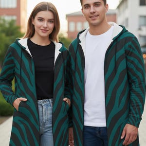 Peut inclure: Deux personnes portant des sweat-shirts &agrave; capuche zipp&eacute;s assortis avec un motif z&eacute;br&eacute; teal et noir. Les sweat-shirts ont une doublure int&eacute;rieure blanche et sont associ&eacute;s &agrave; des jeans et un t-shirt noir ou blanc. L'arri&egrave;re-plan montre des b&acirc;timents et de la verdure.