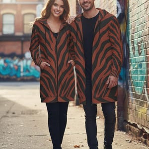 Peut inclure: Deux personnes portant des vestes &agrave; capuche longues assorties avec un motif &agrave; rayures z&eacute;br&eacute;es marron et noir. Les vestes ont une fermeture &eacute;clair sur le devant et des poches. Ils se tiennent dans une rue de la ville.