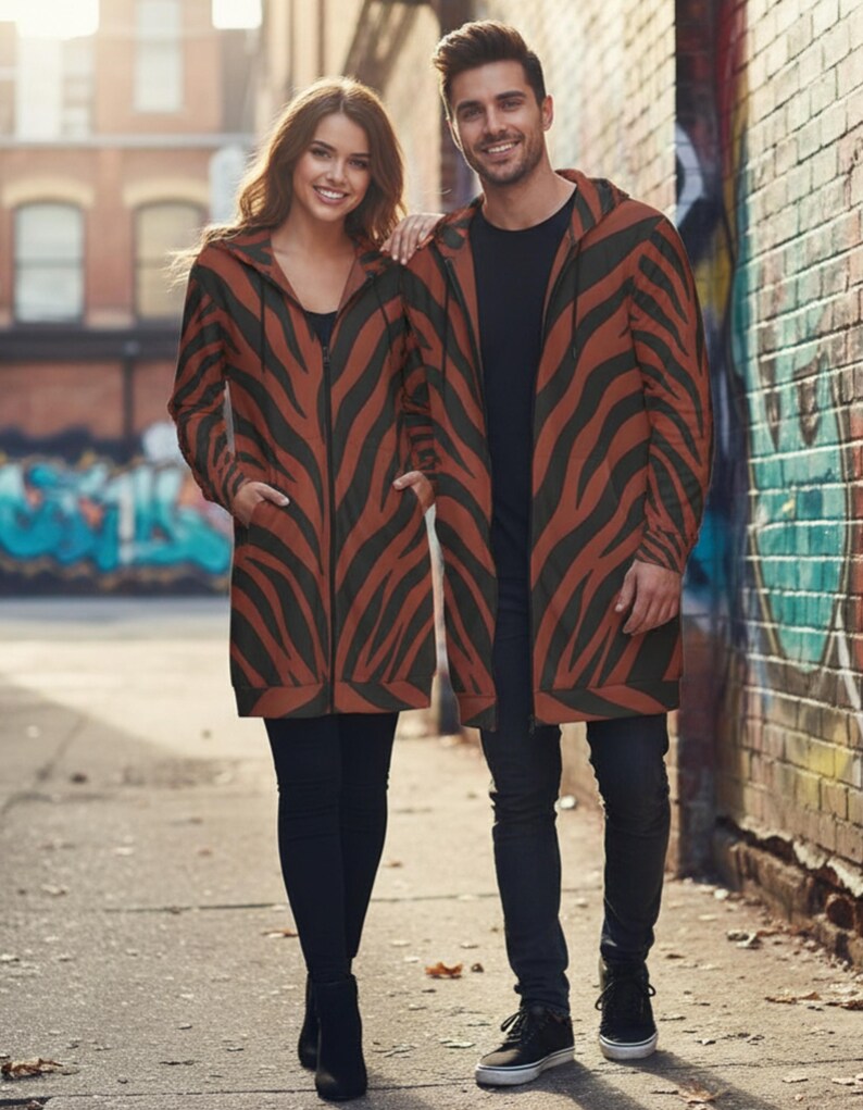 Peut inclure: Deux personnes portant des vestes &agrave; capuche longues assorties avec un motif &agrave; rayures z&eacute;br&eacute;es marron et noir. Les vestes ont une fermeture &eacute;clair sur le devant et des poches. Ils se tiennent dans une rue de la ville.