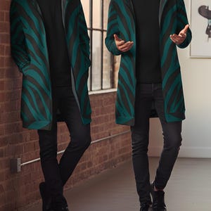 Peut inclure: Longue veste &agrave; capuche avec un motif z&eacute;br&eacute; noir et vert canard. La veste est port&eacute;e sur un t-shirt noir et un pantalon noir. La personne porte des chaussures noires. L'arri&egrave;re-plan comprend un mur de briques et une fen&ecirc;tre.