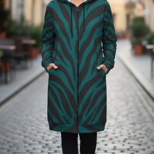 Peut inclure: Longue veste zipp&eacute;e &agrave; capuche avec un motif z&eacute;br&eacute; noir et vert. La veste a une doublure int&eacute;rieure blanche dans la capuche et des poches sur le devant. La personne porte un pantalon noir.