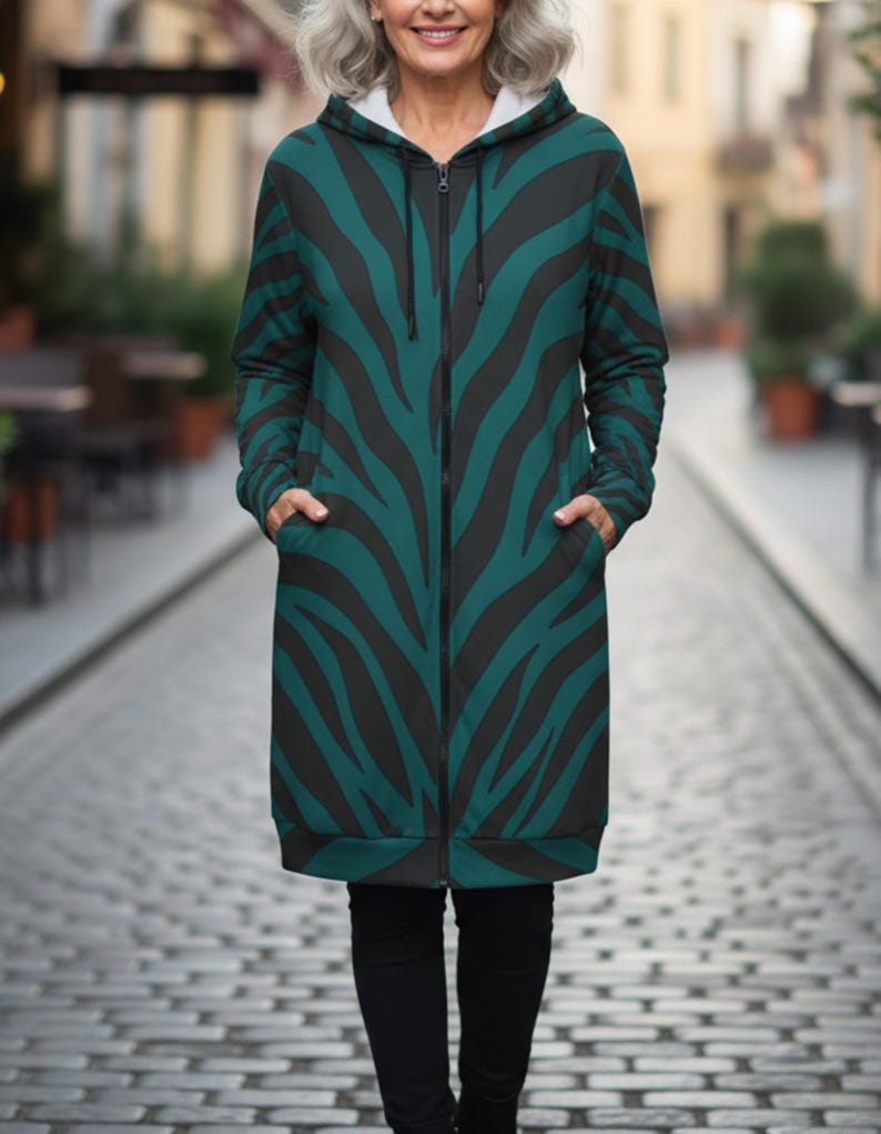 Peut inclure: Longue veste zipp&eacute;e &agrave; capuche avec un motif z&eacute;br&eacute; noir et vert. La veste a une doublure int&eacute;rieure blanche dans la capuche et des poches sur le devant. La personne porte un pantalon noir.