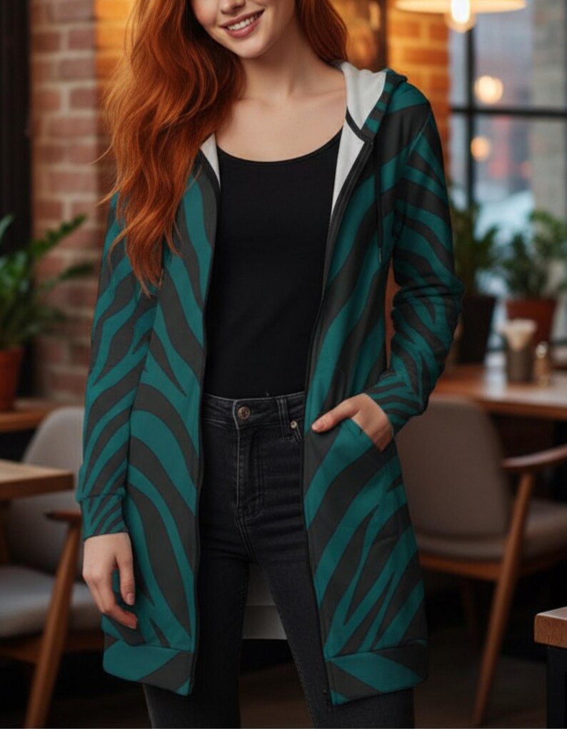 Peut inclure: Longue veste &agrave; capuche avec un motif z&eacute;br&eacute; teal et noir. La veste a une doublure int&eacute;rieure blanche et une fermeture &eacute;clair sur toute la longueur. La personne porte un haut noir et un jean noir. La veste a des poches.