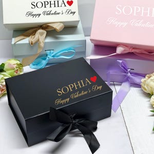 May include: Gift boxes in white, pink, and black, each with a satin ribbon and the name "Sophia" and "Happy Valentine's Day" printed on the lid. The boxes are in various sizes and colors, perfect for Valentine's Day.