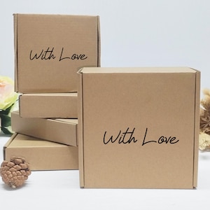 May include: Several small, brown cardboard boxes are stacked and arranged. The boxes have a square shape and are printed with the words "With Love" in a handwritten style. The boxes are plain and simple.