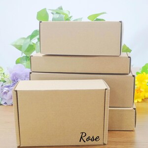 May include: A stack of rectangular, brown cardboard boxes. The boxes are arranged in a neat pile, with the top box slightly offset. The word "Rose" is printed in a cursive font on the front of the bottom box.