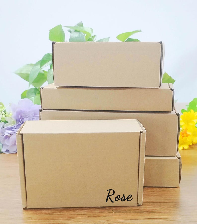 May include: A stack of rectangular, brown cardboard boxes. The boxes are arranged in a neat pile, with the top box slightly offset. The word "Rose" is printed in a cursive font on the front of the bottom box.
