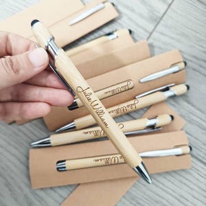 May include: Bamboo pens with silver detailing and black stylus tips, each engraved with the name "Julie William". The pens are presented in individual cardboard packaging, offering a natural and elegant appearance.