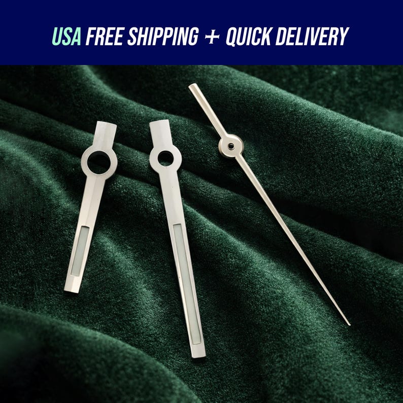 May include: Three silver watch hands on a dark green velvet surface. Two hands have a circular opening and a rectangular section. The third hand is long and thin with a circular detail at the end. Text at the top reads "USA FREE SHIPPING + QUICK DELIVERY".