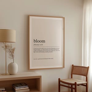 a minimalist living space with a wooden chair, a white lamp, and a framed definition of 'bloom' hanging on the wall.