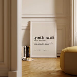 a framed definition of "Spanish mastiff" on a wall, with a bookshelf and a yellow ottoman in the foreground.